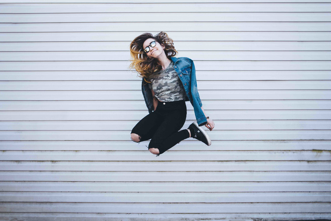 A smiling teenager jumping in the air in front of a white wall